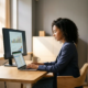 Junge Fachkraft am modernen Schreibtisch analysiert Finanzdokumente auf Laptop mit Diagrammen auf zweitem Monitor.