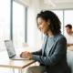 Junge Fachkraft in Business-Casual analysiert Finanzdaten auf Laptop im modernen Büro mit Panoramafenstern und Tageslicht.