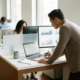 Fachkraft analysiert Finanzdaten auf Laptop im modernen Büro, zweiter Monitor mit Diagrammen, natürliches Licht.