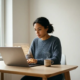 Junge Frau mit mittlerem Fokus studiert am modernen Schreibtisch mit Laptop und dampfendem Kaffee im natürlichen Seitenlicht.