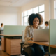 Junge Fachkraft lächelt zuversichtlich am Laptop in einem modernen Steuerbüro mit natürlichem Licht und Kollegen im Hintergrund.
